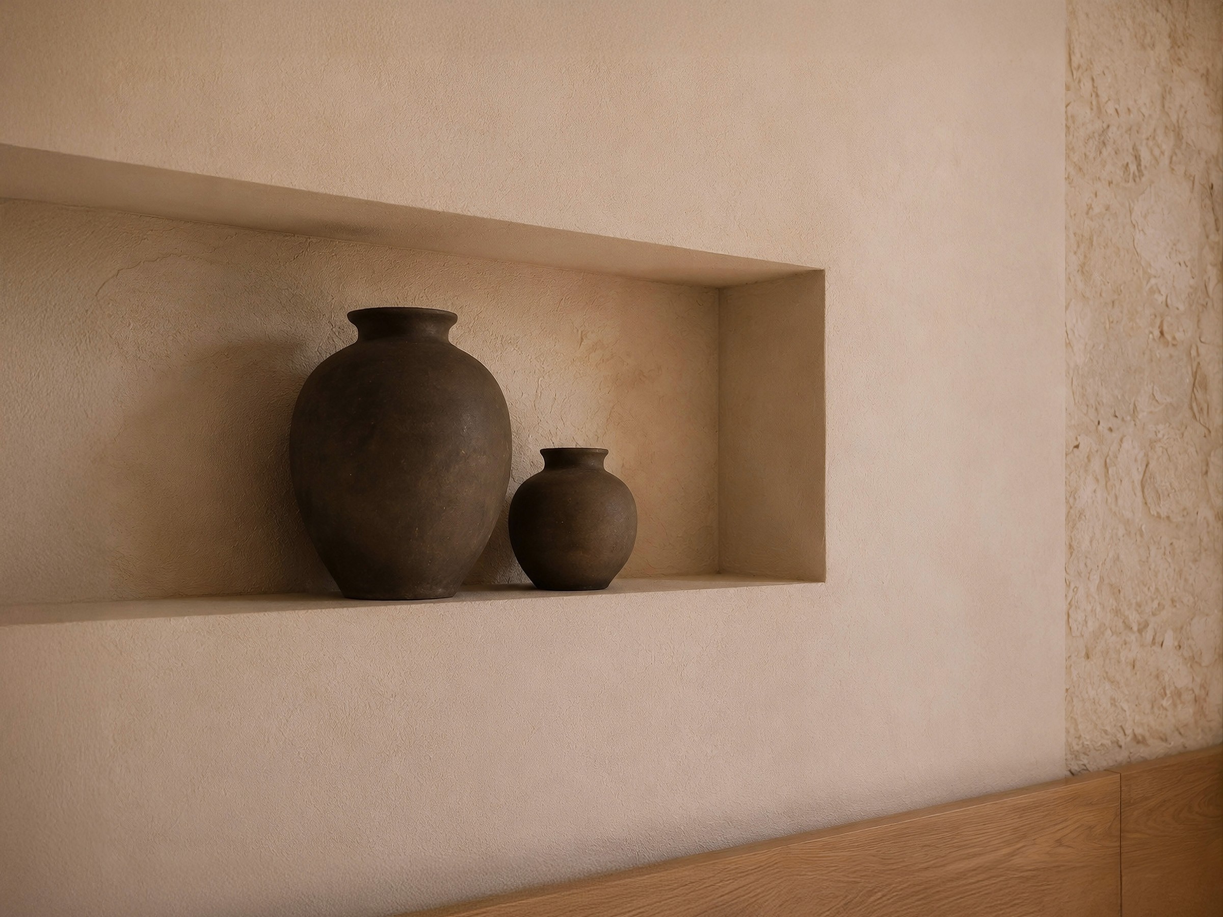 Built-in wall niche beside a textured stone wall, displaying two simple, dark ceramic vases.